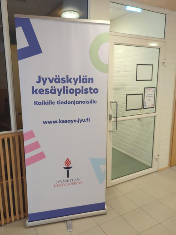 Summer university's office door and roll-up next to the door featuring Summer university's logo: a lit up torch.
