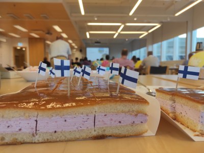 Cake with tiny Finnish flag decorations, classroom with participants in the backround